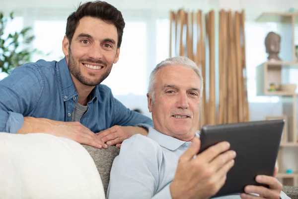 Hombre Sienta Sofá Con Padre Anciano Usando Tableta —  Fotos de Stock