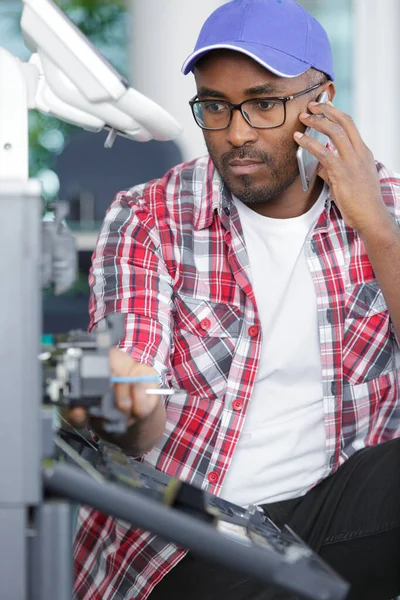 man on telephone next to broken photocopier