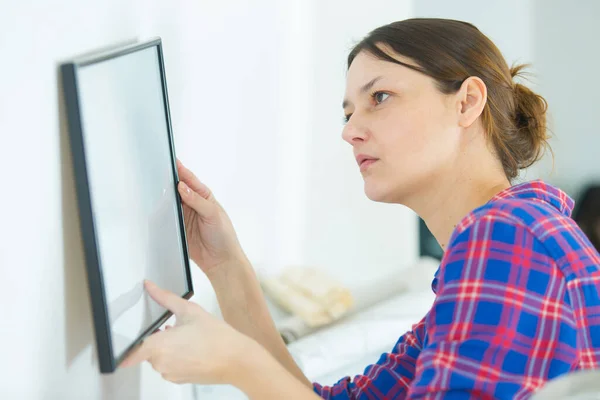 woman hanging picture on wall