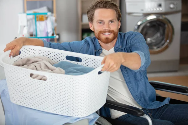 man in wheelchair lifting laundry basket on to ironing board