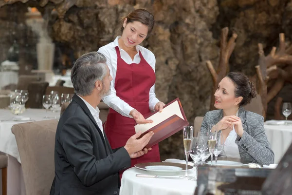 Young Waitress Suggesting Menu Couple Restaurant Stockafbeelding