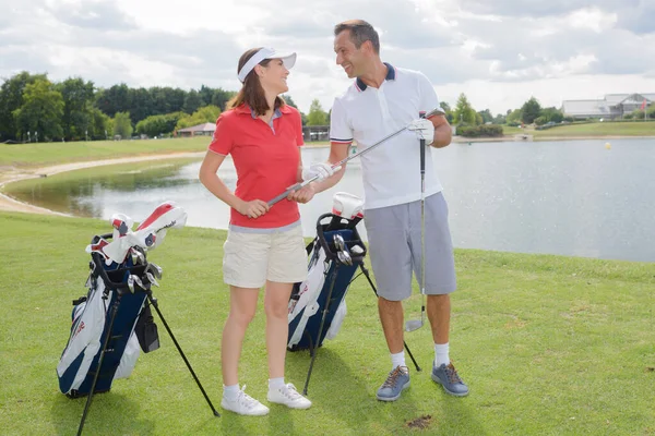 Golfing Couple Smiling Camera Holding Clubs — kuvapankkivalokuva