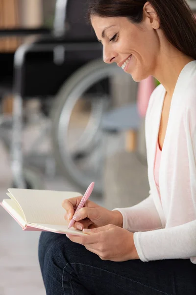 Frau Schreibt Buch Mit Rollstuhl Hintergrund — Stockfoto