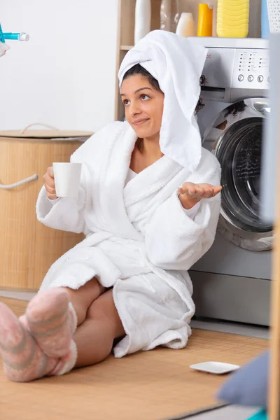 woman in dressing gown making nonchalant gesture by washing machine
