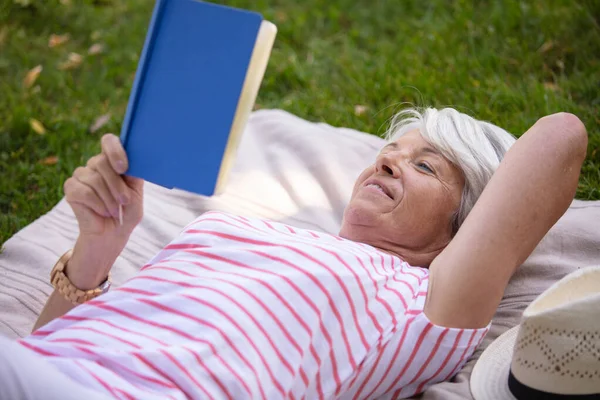 Mulher Sênior Leitura Livro Colocado Grama — Fotografia de Stock