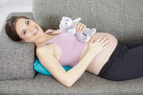 和泰迪熊坐在沙发上笑着的孕妇 — 图库照片