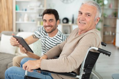 caring son with disabled senior father in wheelchair at home clipart