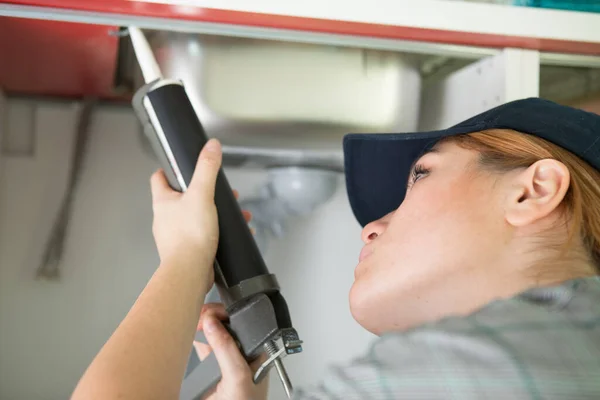 Vrouwelijke Loodgieter Met Behulp Van Caulking Gun Rond Een Gootsteen — Stockfoto