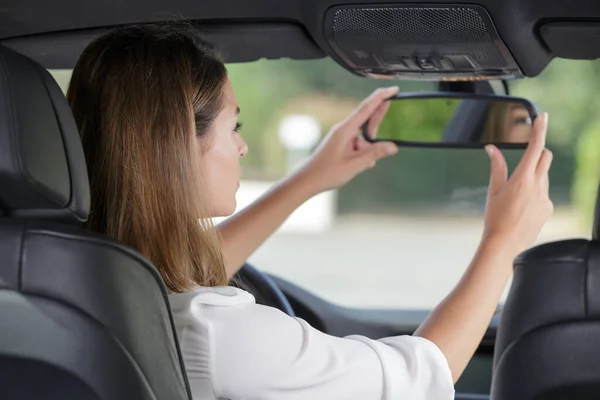 attractive female student adjusting car rear-view mirror during driving lesson