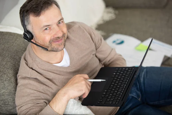 Positive Man Earphones Using Laptop Sitting Sofa —  Fotos de Stock