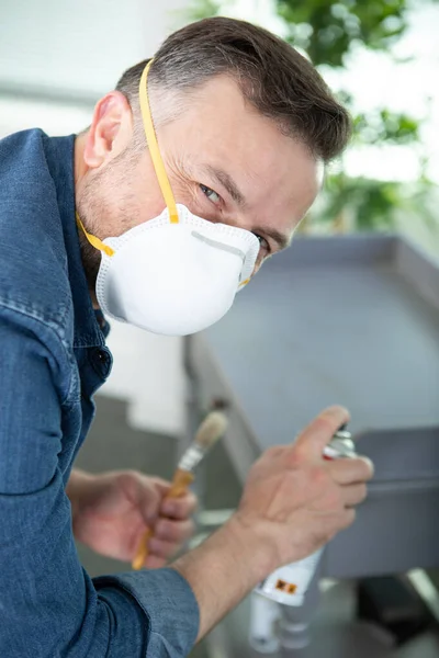 戴口罩的男人用喷雾器粉刷家具 — 图库照片