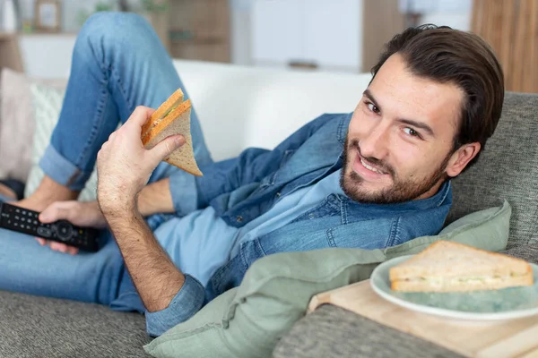 ソファに寝そべってサンドイッチを食べて — ストック写真