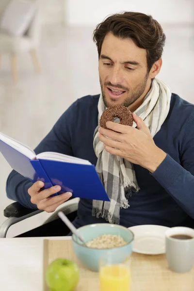 車椅子の男が本を読んでチョコレートドーナツを食べて — ストック写真