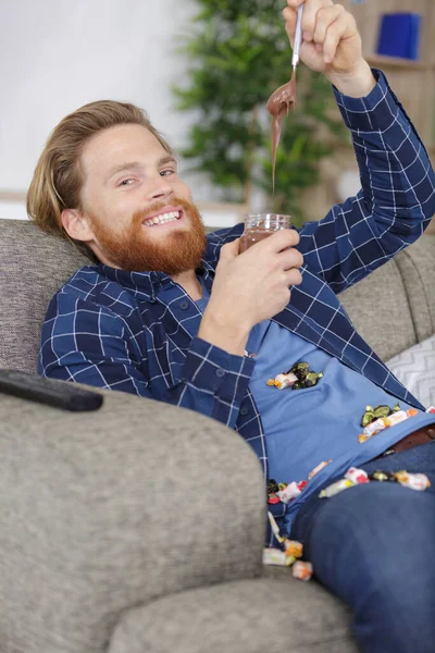 Jovem Homem Comendo Chocolate Enquanto Sentado Sofá Casa — Fotografia de Stock