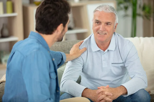 grown son sit on couch relax talking with senior dad