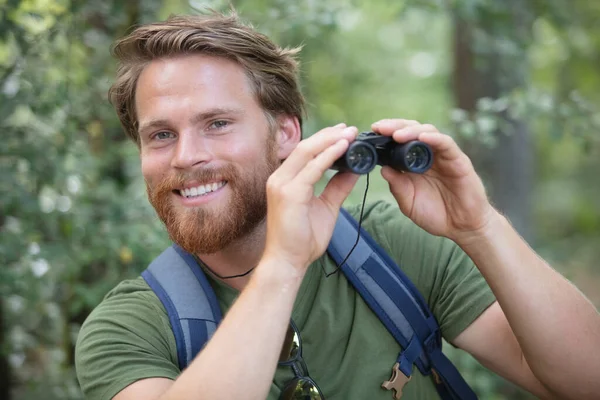 微笑的男性的徒步旅行者在森林中的双筒望远镜的肖像 — 图库照片