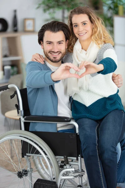 抱着妻子坐在轮椅上的残疾年轻人 — 图库照片