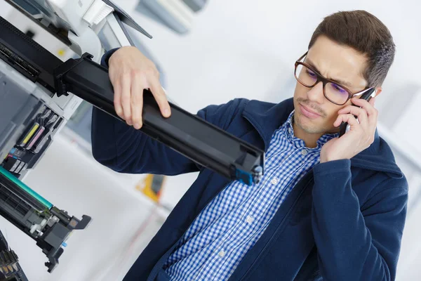 man on telephone next to broken photocopier