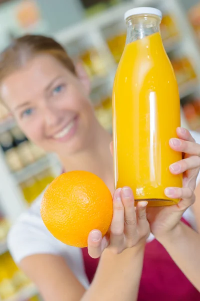 Asistente de tienda sosteniendo naranja y jugo —  Fotos de Stock