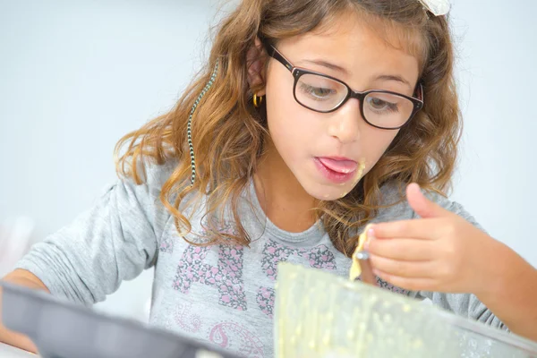 Kleines Mädchen isst Kuchenmix aus der Schüssel — Stockfoto