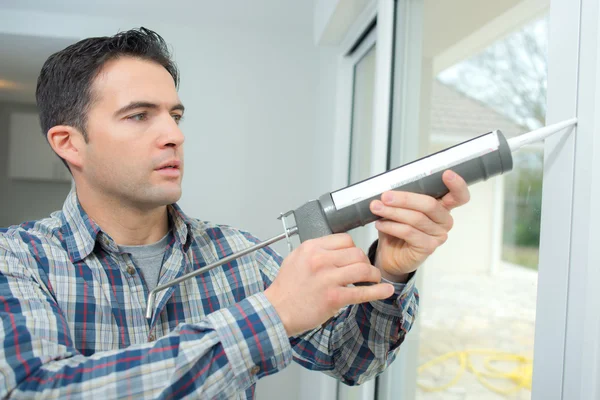 Hombre calafateando una nueva ventana — Foto de Stock