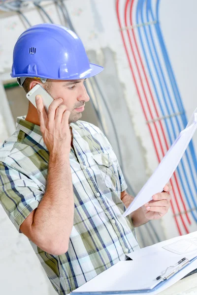 Hombre en el sitio de construcción, mirando planes, hablando por teléfono celular —  Fotos de Stock