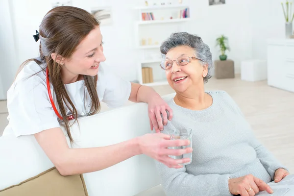 Doctor giving old lady a glass of water — Stock Photo, Image