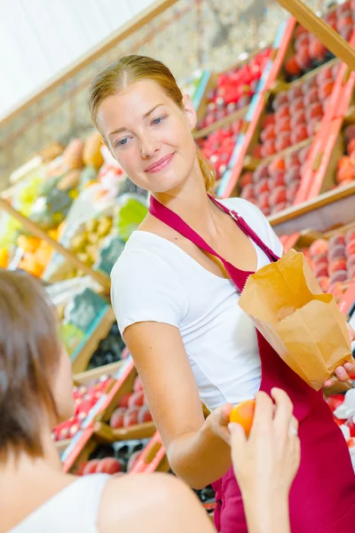 Assistente de loja passando laranja — Fotografia de Stock