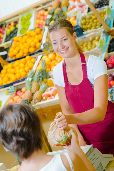 Помощник продавца обслуживает клиентов фруктами и овощами — стоковое фото