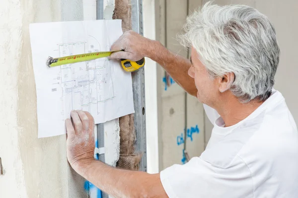 Builder använder ett måttband för att kontrollera byggplaner — Stockfoto
