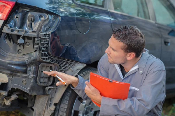 Mechanic holding clipboard assessing car — Stock Photo, Image