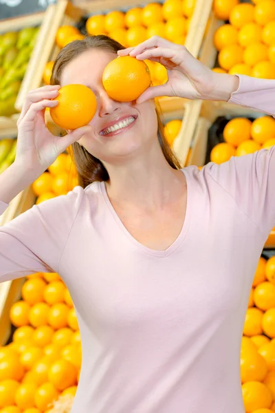 Playful woman covering her eyes with oranges — Stock Photo, Image