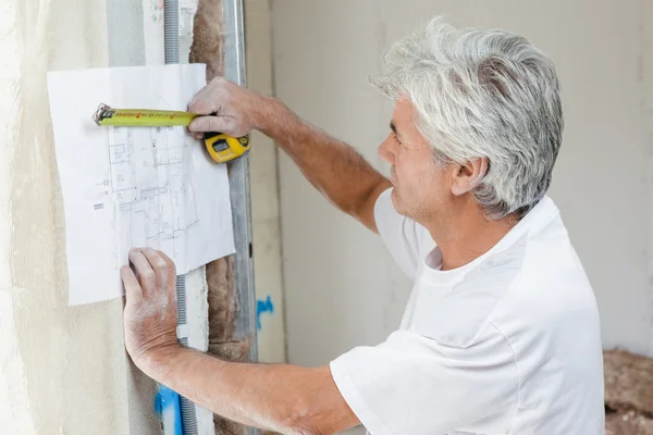 Builder measuring blueprints with tape measure — Stock Photo, Image