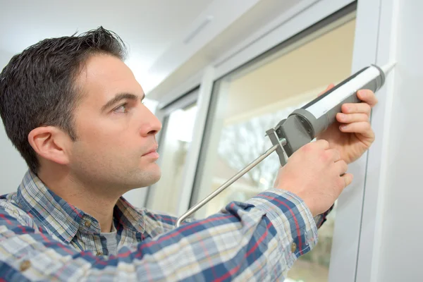 Handyman calafetando uma janela — Fotografia de Stock