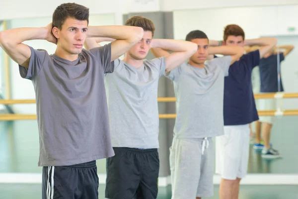 Quatre jeunes hommes faisant de l'exercice, les bras derrière la tête — Photo