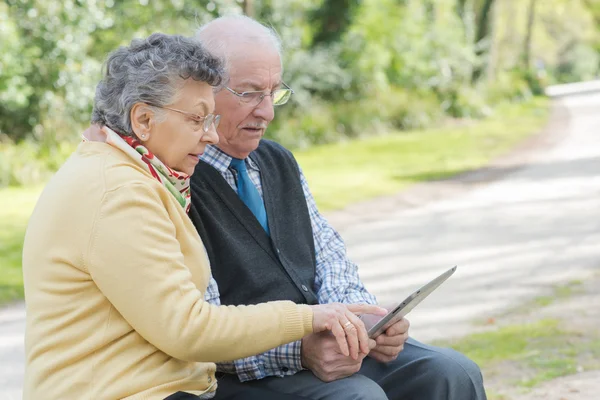 Casal de idosos sentado no banco olhando para tablet — Fotografia de Stock