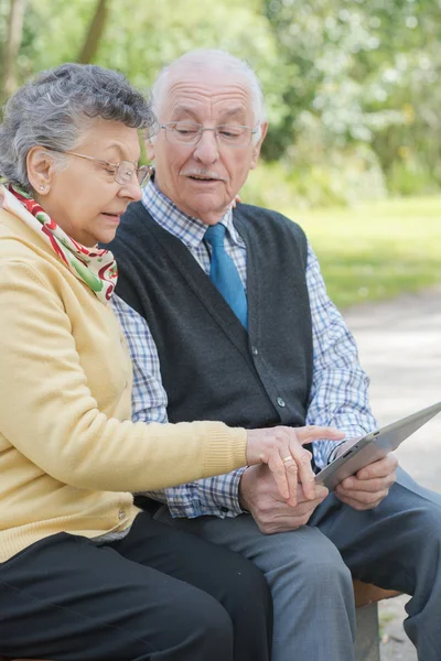 Pareja de ancianos en el parque con una tableta — Foto de Stock