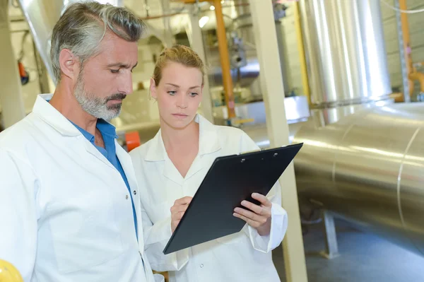 Man and lady in factory looking at clipboard — Stock Photo, Image