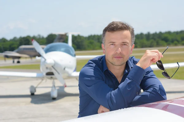 Man holding sunglasses, leaning on aircraft — Stock Photo, Image