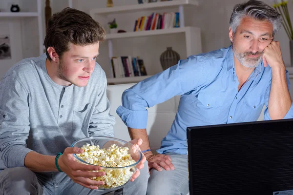 Dois homens assistindo televisão segurando tigela de pipocas — Fotografia de Stock