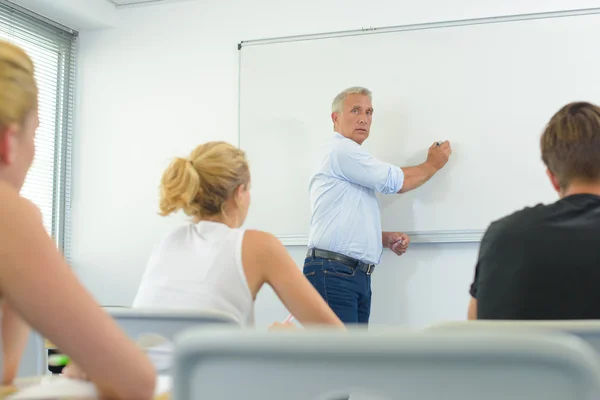 Teacher writing on whiteboard in front of class — Stock Photo, Image