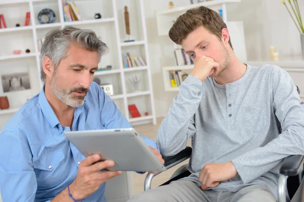 Uomo che mostra lo schermo del tablet al giovane sulla sedia a rotelle — Foto Stock