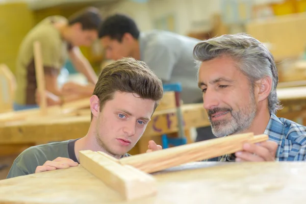 Tischler schaut sich die Arbeit seines Lehrlings an — Stockfoto