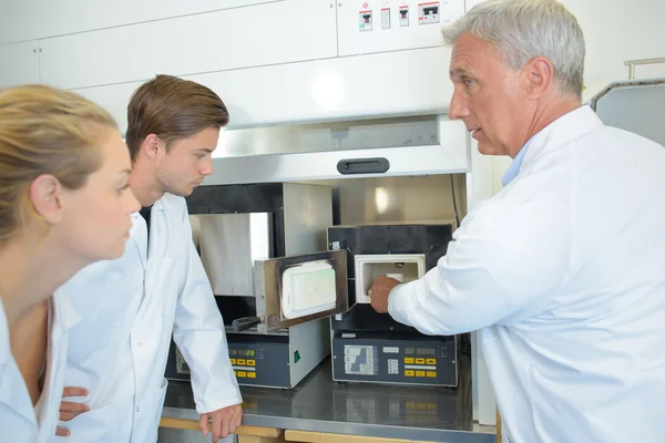 Técnico colocando produto em aparelho, estagiários assistindo — Fotografia de Stock