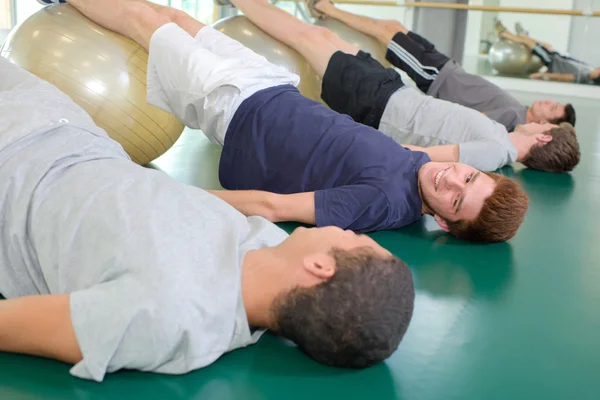 Four men with legs raised on aerobic balls — Stock Photo, Image