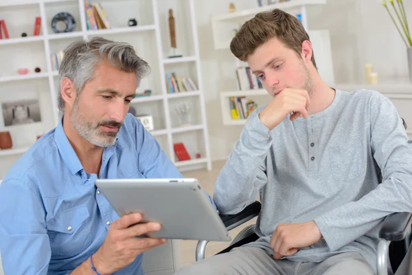 Man showing computer to younger man in wheelchair — Stock Photo, Image