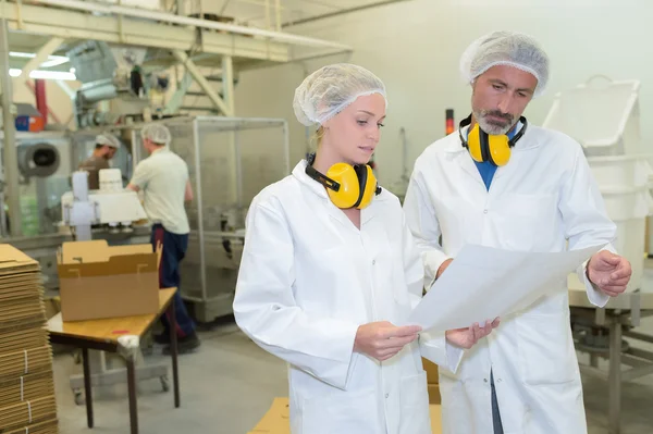 Man and woman in factory holding paperwork — Stock Photo, Image