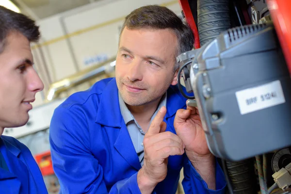 Professor olhando para o motor, dando aviso ao aprendiz — Fotografia de Stock