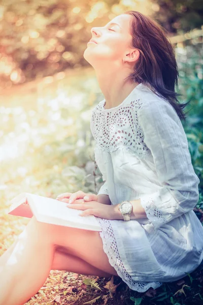 Doordachte vrouw zittend op de grassen in de tuin — Stockfoto