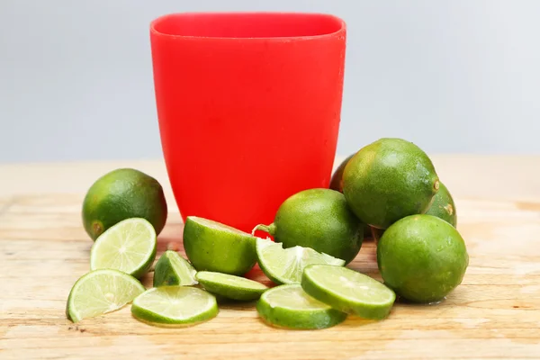 Verre en plastique rouge avec des citrons verts autour — Photo